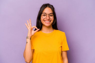 Mor arka planda izole edilmiş genç İspanyol kadın neşeli ve kendinden emin, iyi bir hareket gösteriyor..