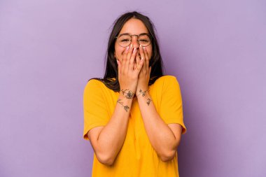 Mor arka planda izole edilmiş genç İspanyol kadın bir şeye gülüyor, elleriyle ağzını kapatıyor..