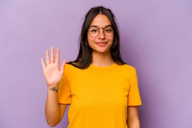 Mor arka planda izole edilmiş genç İspanyol kadın gülümseyerek beş numarayı parmaklarıyla gösteriyor..