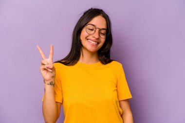 Mor arka planda izole edilmiş genç İspanyol kadın neşeli ve kaygısız parmakları olan bir barış sembolü gösteriyor..