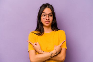 Mor arka plan noktalarında izole edilmiş genç İspanyol kadın iki seçenek arasında seçim yapmaya çalışıyor..