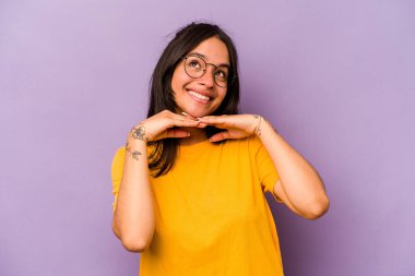 Mor arka planda izole edilmiş genç İspanyol kadın ellerini çenesinin altında tutuyor ve mutlu bir şekilde yan tarafa bakıyor..