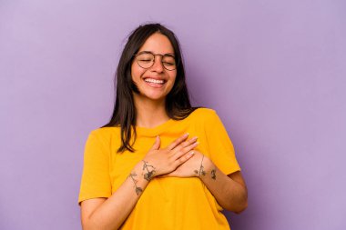 Mor arka planda izole olmuş genç İspanyol kadın gülüyor, elleri yüreğinde, mutluluk kavramında..