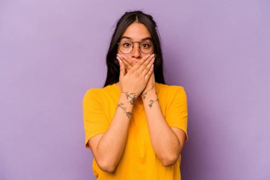 Mor arka planda izole edilmiş genç İspanyol kadın elleri endişeli bir şekilde ağzı örtüyor..