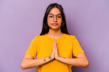 Genç İspanyol kadın mor arka planda izole edilmiş dua ediyor, bağlılık gösteriyor, dindar biri ilahi ilham arıyor..