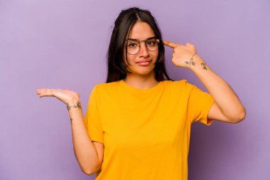 Mor arka planda izole edilmiş genç İspanyol kadın elinde bir ürün tutuyor..