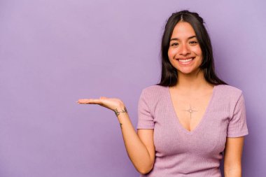 Mor arka planda izole edilmiş genç İspanyol kadın bir avuç içinde fotokopi alanı ve belinde bir el daha gösteriyor..