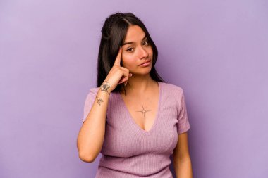 Mor arka planda izole edilmiş genç İspanyol bir kadın şakağı parmağıyla işaret ediyor, düşünüyor ve bir göreve odaklanıyor..