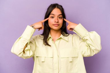 Mor arka planda izole edilmiş genç İspanyol kadın bir işe odaklanmış, işaret parmaklarını işaret ediyor..