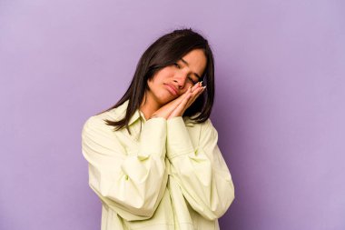 Mor arka planda izole edilmiş genç İspanyol kadın esniyor. Ağzı eliyle kapatan yorgun bir hareket sergiliyor..