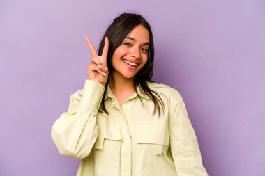 Mor arka planda izole edilmiş genç İspanyol kadın iki numarayı parmaklarıyla gösteriyor..