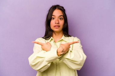 Mor arka plan noktalarında izole edilmiş genç İspanyol kadın iki seçenek arasında seçim yapmaya çalışıyor..