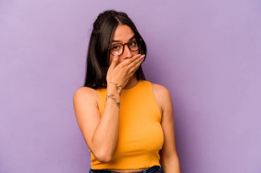 Mor arka planda izole edilmiş genç İspanyol kadın elleri endişeli bir şekilde ağzı örtüyor..