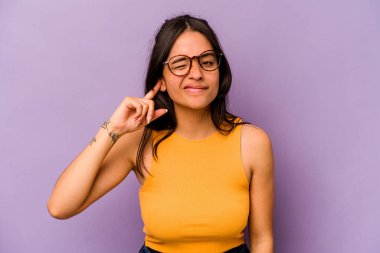 Mor arka planda izole edilmiş, parmaklarıyla kulaklarını kapatan, gürültülü bir ortam tarafından stresli ve çaresiz genç İspanyol kadın..