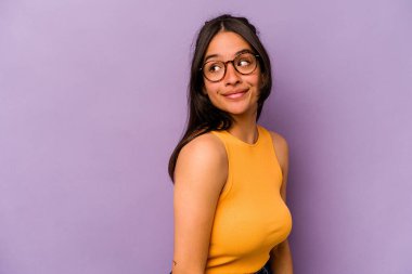 Mor arka planda soyutlanmış genç İspanyol kadın gülümseyen, neşeli ve keyifli bir kenara bakıyor..