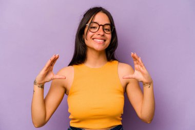 Mor arka planda izole edilmiş genç İspanyol kadın elinde avuç içi bir şeyle kameraya sunuyor..