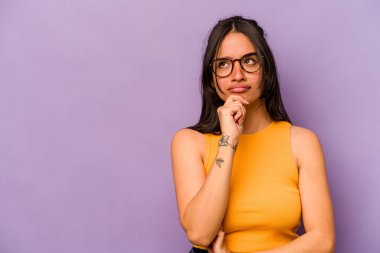 Mor arka planda izole edilmiş genç İspanyol kadın şüpheli ve şüpheci bir ifadeyle yana bakıyor..