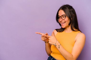 Genç İspanyol kadın mor arka planda izole edilmiş başparmak uzakta, gülüyor ve kaygısız.
