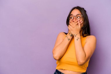 Mor arka planda izole edilmiş genç bir İspanyol kadın. Bir fotokopi odasına dikkatlice bakıyor. Ağzını eliyle kapatıyor..