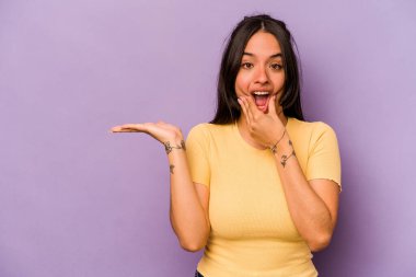 Mor arka planda izole edilmiş genç İspanyol kadın avuç içinde fotokopi alanı tutuyor, el üstünde tutuyor. Şaşırmış ve mutlu..