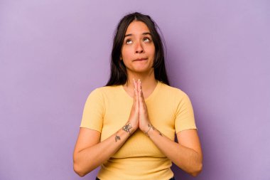 Mor arka planda izole edilmiş genç İspanyol kadın el ele tutuşup ağzının kenarında dua ediyor, kendinden emin hissediyor..