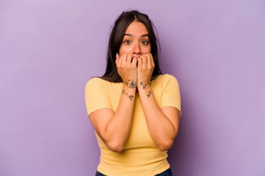 Mor arka planda izole edilmiş, tırnak yiyen, gergin ve endişeli genç bir kadın..