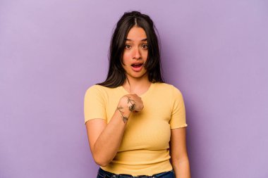 Mor arka planda izole edilmiş genç İspanyol kadın parmağını göstererek şaşırdı, geniş bir gülümsemeyle..