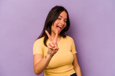 Mor arka planda izole edilmiş genç İspanyol kadın iki numarayı parmaklarıyla gösteriyor..