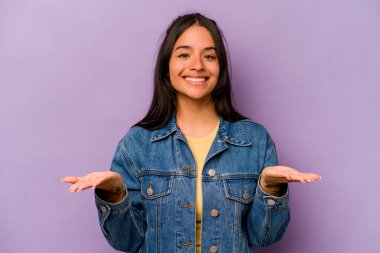 Mor arka planda izole edilmiş genç İspanyol kadın kollarıyla ölçeği yapıyor, mutlu ve kendinden emin hissediyor..