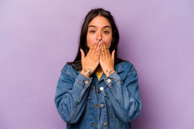 Mor arka planda izole edilmiş genç İspanyol kadın elleri endişeli bir şekilde ağzı örtüyor..