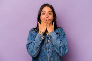 Mor arka planda izole edilmiş genç İspanyol kadın şok olmuş, ağzı ellerle kaplanmış, yeni bir şey keşfetmeye hevesli..