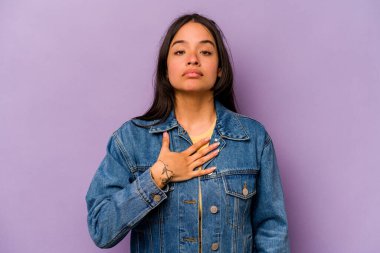 Mor arka planda izole edilmiş genç İspanyol kadın yemin ediyor, elini göğsüne koyuyor..