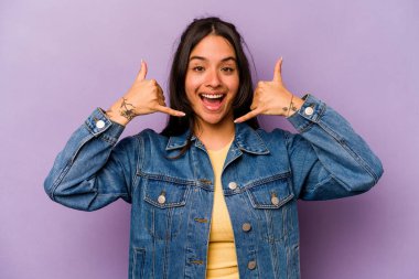 Mor arka planda izole edilmiş genç İspanyol kadın parmaklarıyla bir cep telefonu hareketi gösteriyor..