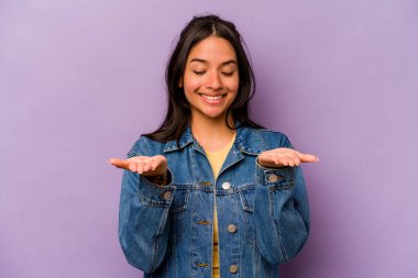 Mor arka planda izole edilmiş genç İspanyol kadın elinde avuç içi bir şeyle kameraya sunuyor..