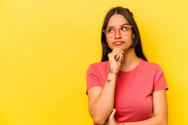 Sarı arka planda izole edilmiş genç İspanyol kadın şüpheli ve şüpheci bir ifadeyle yana bakıyor..
