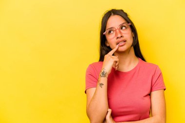 Sarı arka planda izole edilmiş genç İspanyol kadın şüpheli ve şüpheci bir ifadeyle yana bakıyor..