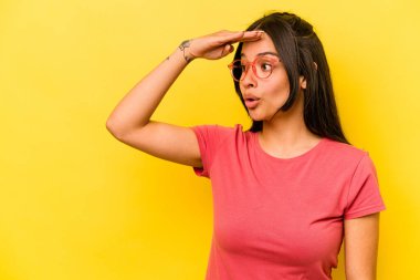 Sarı arka planda izole edilmiş genç İspanyol kadın uzaklara bakıyor ve elini alnına koyuyor..