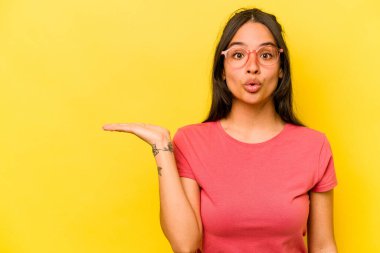 Sarı arka planda izole edilmiş genç İspanyol kadın avuç içi fotokopi alanını tutmaktan etkilenmiş..