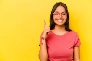 Sarı arka planda izole edilmiş genç İspanyol kadın bir numarayı parmağıyla gösteriyor..