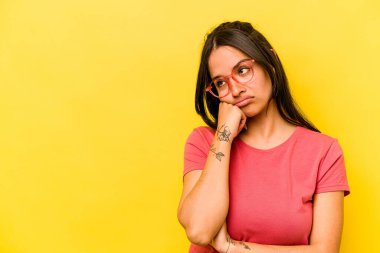 Sarı arka planda izole edilmiş genç İspanyol kadın üzgün ve dalgın hissediyor, kopyalama alanına bakıyor..