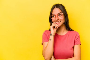Sarı arka planda izole edilmiş genç İspanyol kadın rahatlamış bir şeyin fotokopi odasına baktığını düşünüyor..