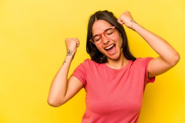 Sarı arka planda izole edilmiş genç İspanyol kadın zaferden sonra yumruk kaldırıyor, kazanan konsept..