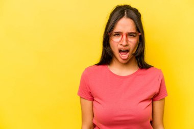 Sarı arka planda izole edilmiş genç İspanyol kadın çok kızgın, öfkeli, hayal kırıklığına uğramış.