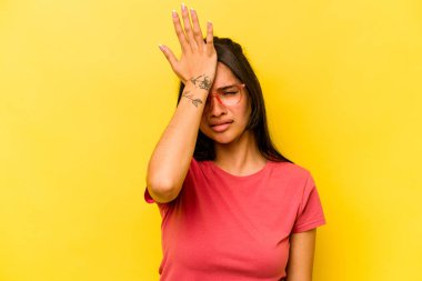 Sarı arka planda izole edilmiş genç İspanyol kadın bir şeyi unutuyor. Alnına avuç içi ile vuruyor ve gözlerini kapıyor..