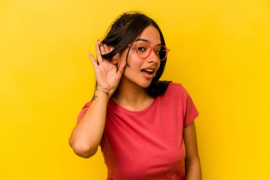 Sarı arka planda izole edilmiş genç İspanyol kadın bir dedikoduyu dinlemeye çalışıyor..