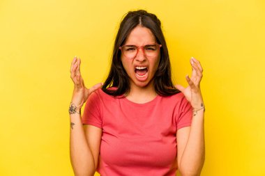Sarı arka planda izole edilmiş genç İspanyol kadın öfkeyle bağırıyor..
