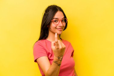 Sarı arka planda izole edilmiş genç İspanyol kadın sanki seni davet ediyormuş gibi seni işaret ediyor..
