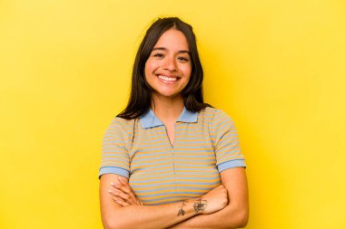 Sarı arka planda izole edilmiş, kendinden emin, kararlılıkla kollarını kavuşturan genç İspanyol kadın..