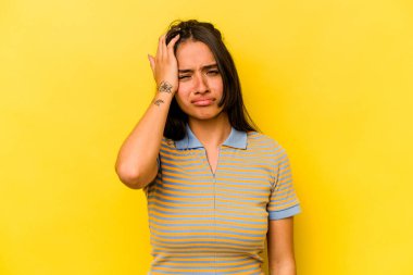 Sarı arka planda izole edilmiş genç İspanyol kadın yorgun ve uykulu ellerini başının üstünde tutuyor..