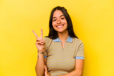 Sarı arka planda izole edilmiş genç İspanyol kadın iki numarayı parmaklarıyla gösteriyor..